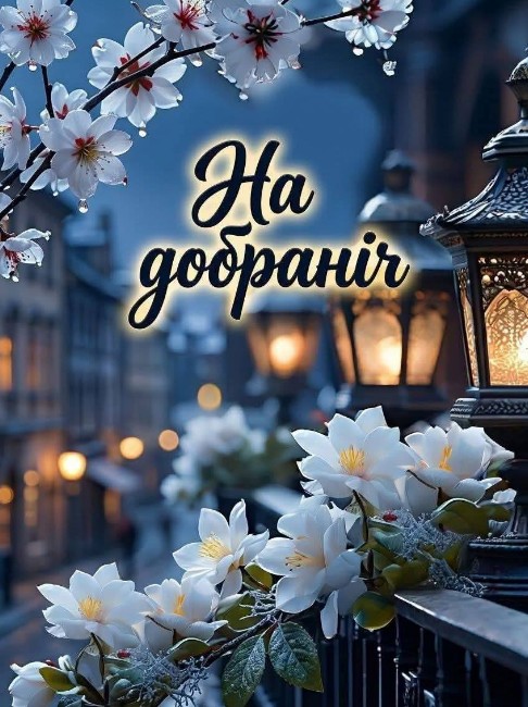 Красива вечірня листівка з написом На добраніч, білі квіти на фоні вуличних ліхтарів та затишного міста